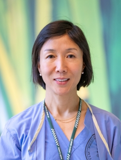 Smiling woman with short black hair wearing blue scrubs and a blue lanyard with a green background