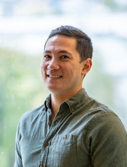 Smiling man with short dark hair standing in front of a large window