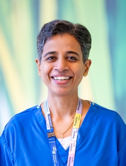 Woman smiling with short dark hair, wearing scrubs and a colorful lanyard with a green background