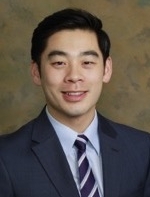 Man smiling with short black hair, wearing a dark suit, blue shirt and stripped tie