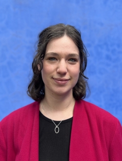 Woman with should length wavy hair wearing a red sweater with a blue background