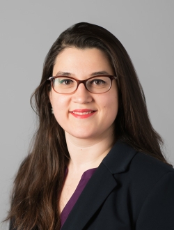 Woman smiling with long dark hair, wearing glasses and a dark jacket.