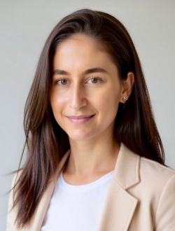 Woman with long dark brown hair, wearing a beige blazer over a white shirt