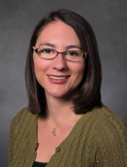 Woman smiling with shoulder length dark brown hair wearing glasses and a green sweater