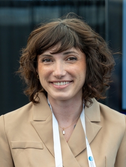 Smiling woman with shoulder length brown wavy hair wearing a tan jacket.