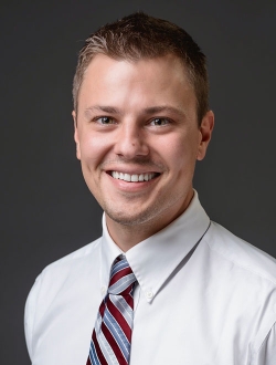 Smiling man with short brown hair wearing a shirt and tie.