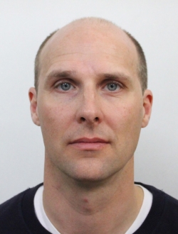 Man with short brown hair wearing a dark sweater.