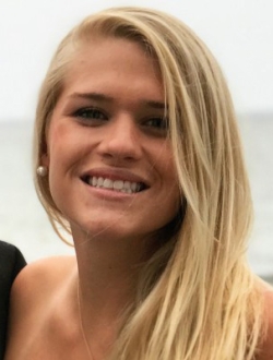 Smiling woman with long blond hair with the ocean in the background.