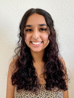 Smiling woman with long dark brown wavy hair in front of a white background.