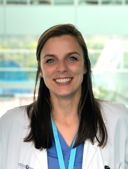 Smiling woman with long dark brown hair wearing a white lab coat.