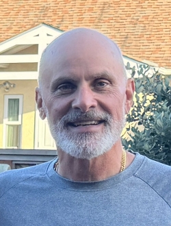 Man with a short white beard wearing a gray shirt.