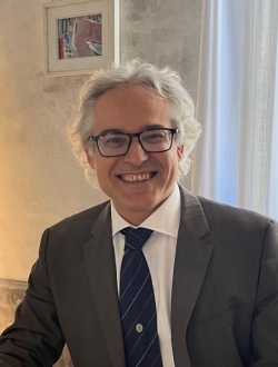 Smiling man with glasses and light gray hair wearing a suit and tie.