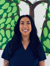 Smiling woman with long black hair wearing dark blue scrubs.