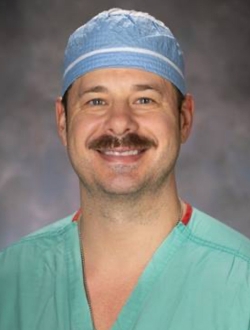 Smiling man with mustache, wearing srubs.