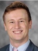 Smiling man with short light brown hair wearing a suit and tie.