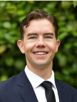 Smiling man with short brown hair wearing a suit and tie.