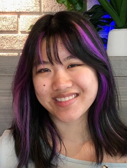 Smiling woman with long black hair with purple highlights.