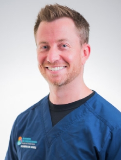 Smiling man with short blond hair wearing blue scrubs.