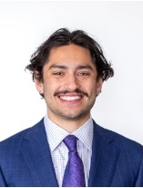 Smiling man with dark hair and mustache wearing a blue suite and tie.