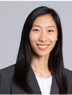 Smiling woman with long black hair wearing a dark jacket over a white top.