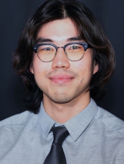 Man with dark hair wearing glasses, a gray shirt and dark tie.
