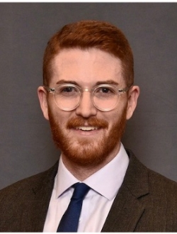 Smiling man with short brown hair and beard, wearing a suite and tie.