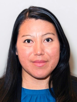 Woman with long black hair wearing a blue top under a black jacket.