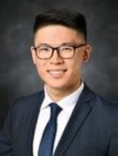 Smiling man with short black hair wearing glasses and a suit and tie.