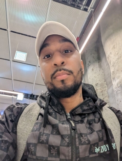 Man with a short black beard wearing a jacket and cap.