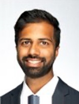 Smiling man with dark hair and beard wearing a suit and tie.
