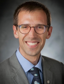 Man with short brown hair and glasses wearing a suit and tie.
