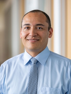 Man with short dark hair wearing a blue shirt and tie.