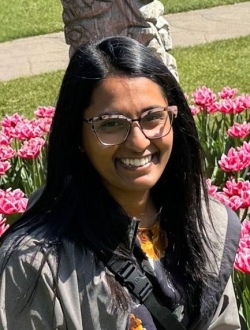 Smiling woman with long black hair wearing glasses with flowers in the background.