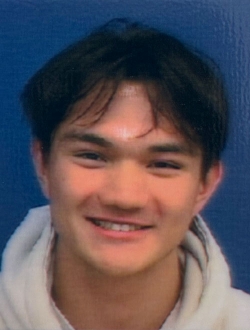 Smiling young man with black hair wearing a light gray hoodie with a blue background.