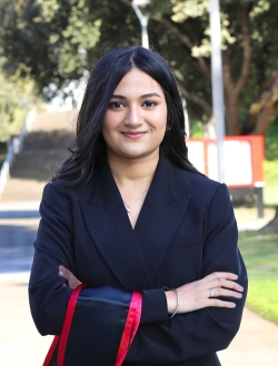 Woman with long black hair wearing a black jacket with her arms crossed.