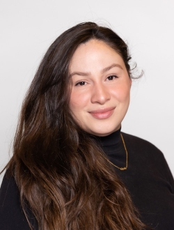 Woman with long wavy dark brown hair wearing a black turtle neck sweater.