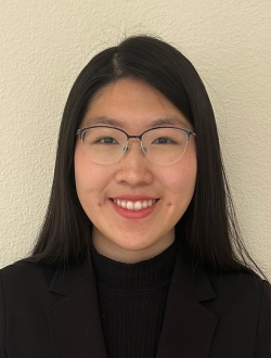 Smiling woman with long black hair wearing glasses and a black sweater.
