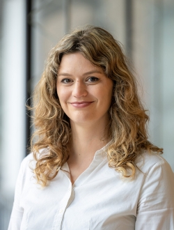 Woman with long wavy blonde hair wearing a light colored collard shirt..