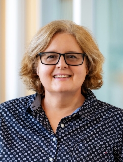 Woman with light shoulder length hair wearing glasses and a navy and white checked shirt..