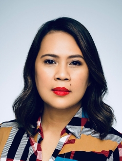 Woman with shoulder length wavy black hair wearing a colorful shirt.