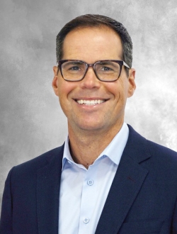 Smiling man with glasses and short dark hair wearing a suit jacket and collared shirt.
