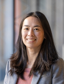 Smiling woman with long black hair wearing a gray jacket.