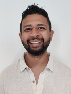 Smiling man with short black hair and beard wearing a white buttoned shirt.
