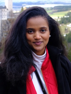 Smiling woman with long dark brown hair wearing a red coat over a white turtleneck.