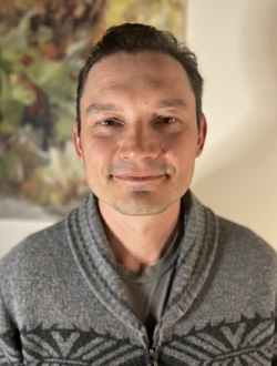 Man with short brown hair wearing a sweater.