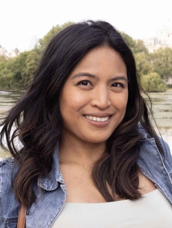 Smiling woman with long dark brown hair with trees in the background.