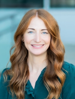 Smiling woman with long wavy red hair wearing a green shirt.