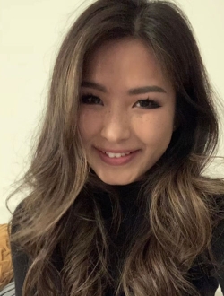 Smiling woman with long wavy brown hair wearing a black turtleneck sweater.