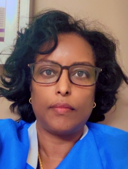 Woman with wavy shoulder-length dark brown hair wearing glasses and scrubs.
