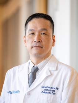 Man with short black hair wearing a lab coat and tie.